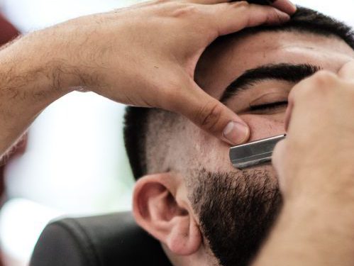 Young man get a razor line on his beard at the barbershop